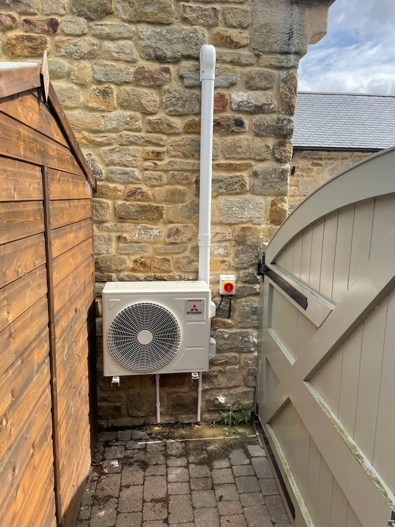 Outdoor air conditioning unit mounted against a stone wall beside a garden gate