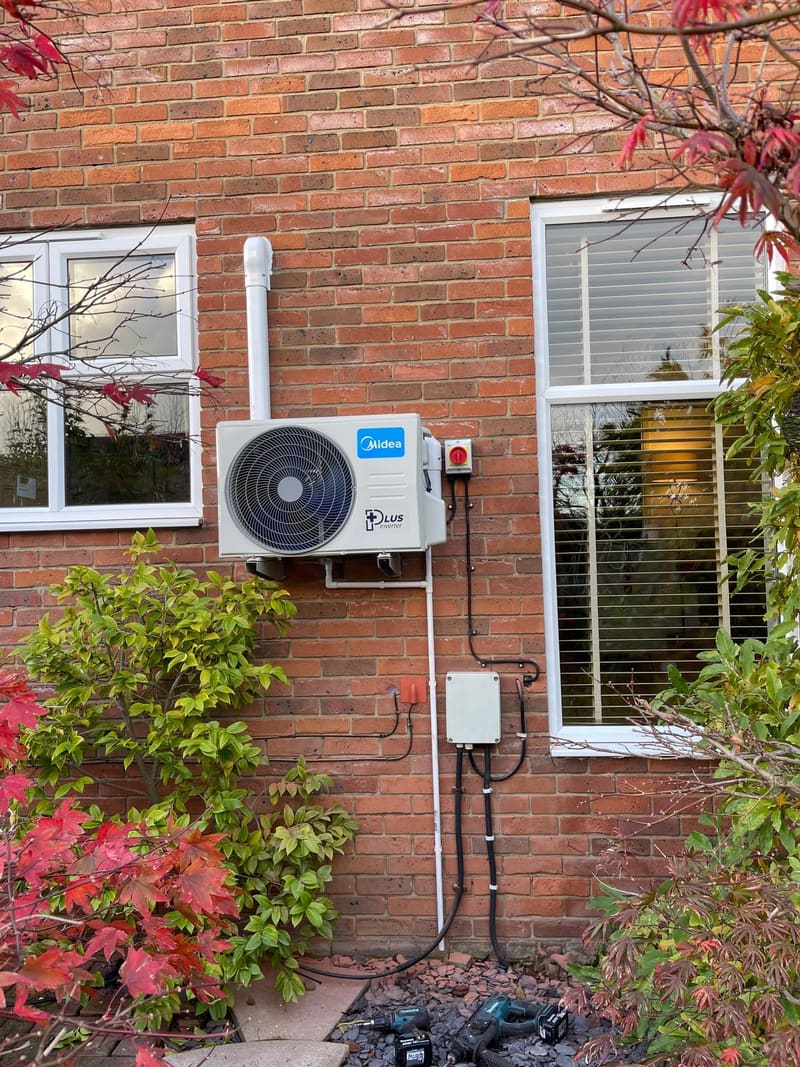 Outdoor air conditioning unit installed on a wall bracket beside a window with tidy pipe trunking