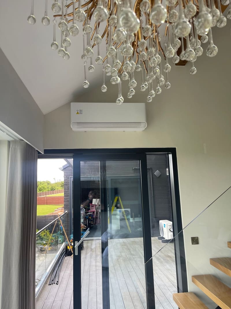 White wall-mounted air conditioner high on the wall of a vaulted living space with glazed doors