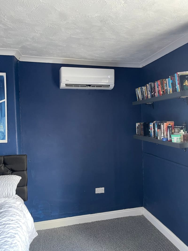 Wall-mounted air conditioner in a bedroom with a navy blue wall