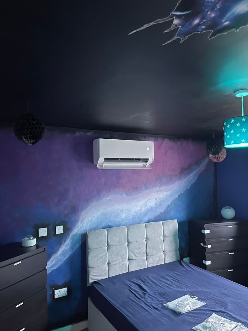 Wall-mounted air conditioner above a bed in a bedroom with a galaxy mural