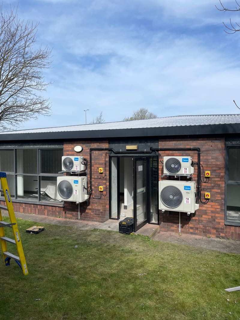 Four air conditioning condenser units mounted either side of the entrance to a single-storey commercial building
