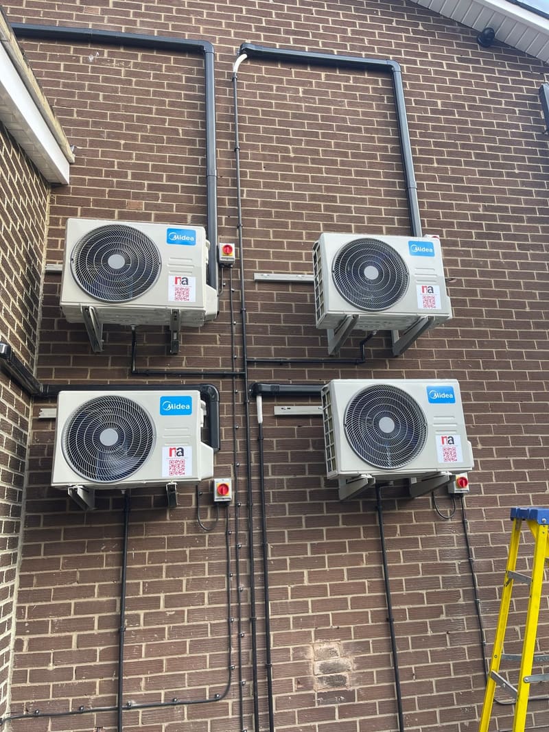 Four multi split air conditioning outdoor units mounted on a brick wall with neat vertical pipe runs