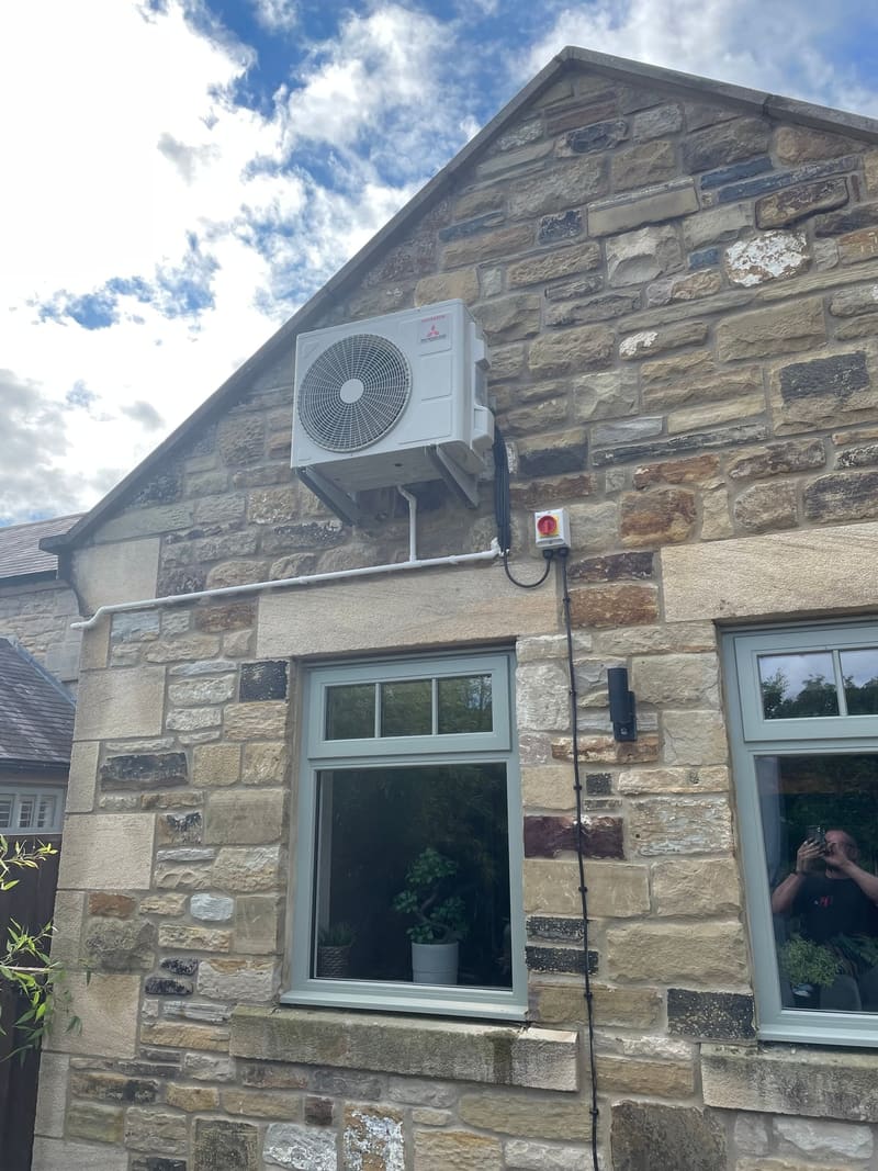 Air conditioning outdoor unit installed high on the gable of a period stone cottage