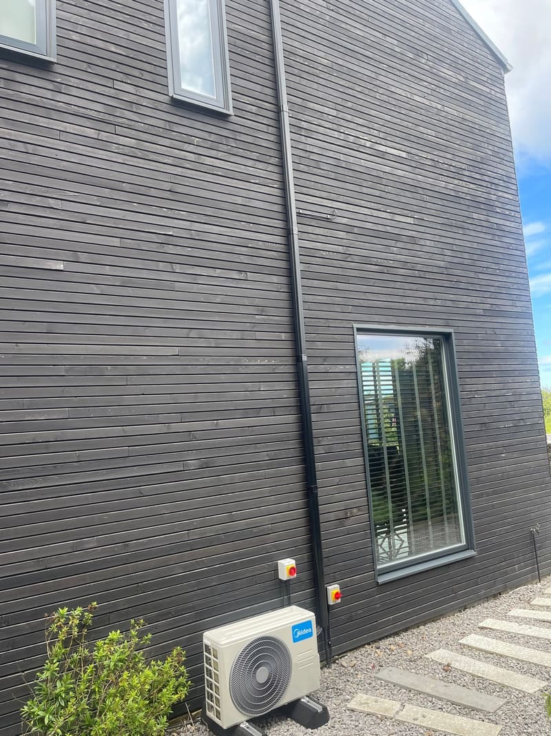 Air conditioning outdoor unit installed beside a window on a modern timber-clad coastal home
