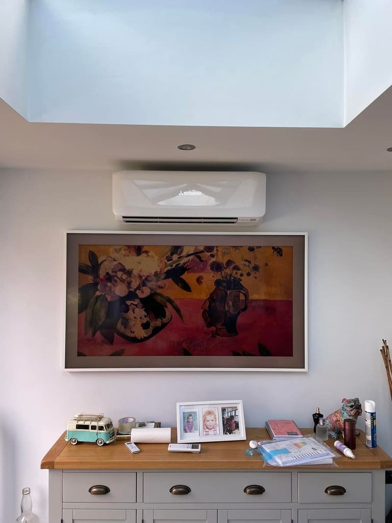 Wall-mounted air conditioner installed above a framed painting in a living room