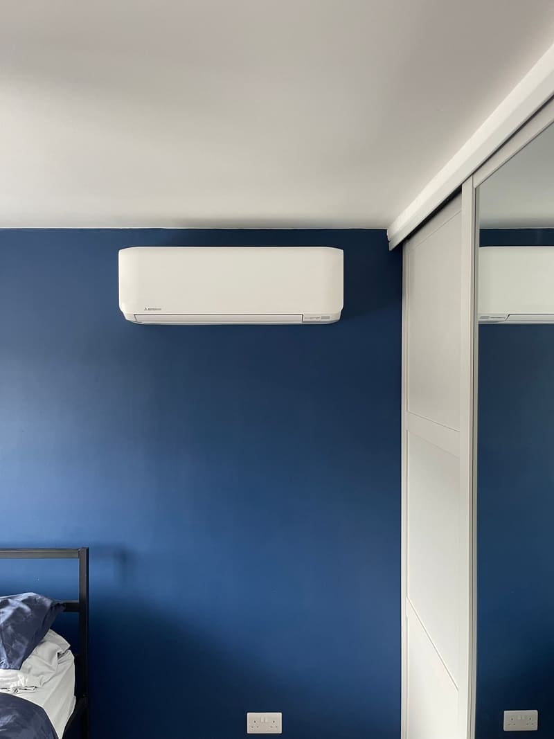 Newly installed white wall-mounted air conditioning unit on a navy blue feature wall